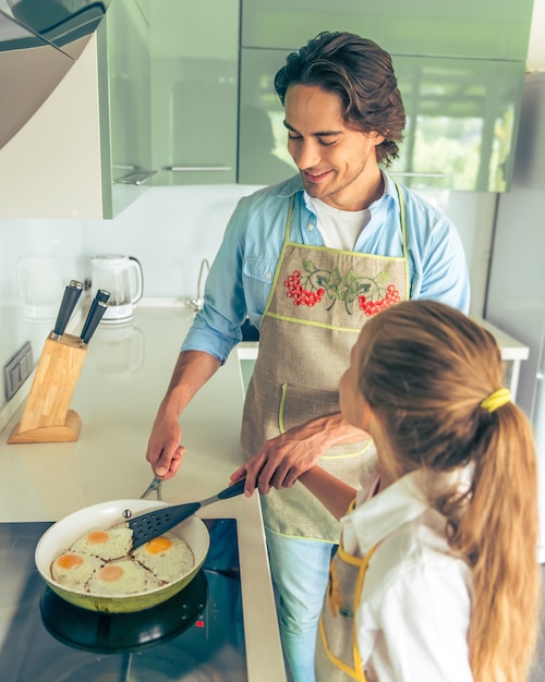 La ragazza e suo padre bello stanno cucinando le uova fritte.