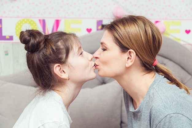 女の子と彼女の母親はソファで家で楽しい時間を過ごしています。幸せな家族の概念。