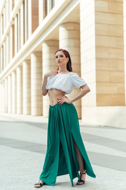 A girl in her thirties with red hair next to a fancy building in the summertime.