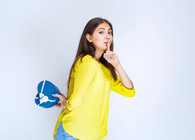 Girl hiding the blue heart shape gift box behind herself.