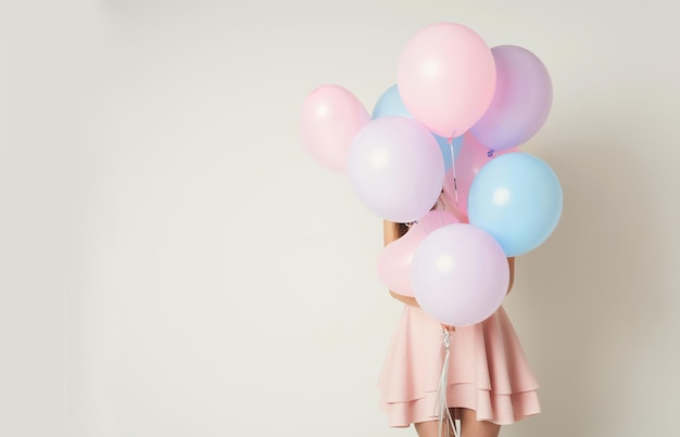 Девушка прячется за огромной связкой воздушных шаров, белый фон, копией пространства