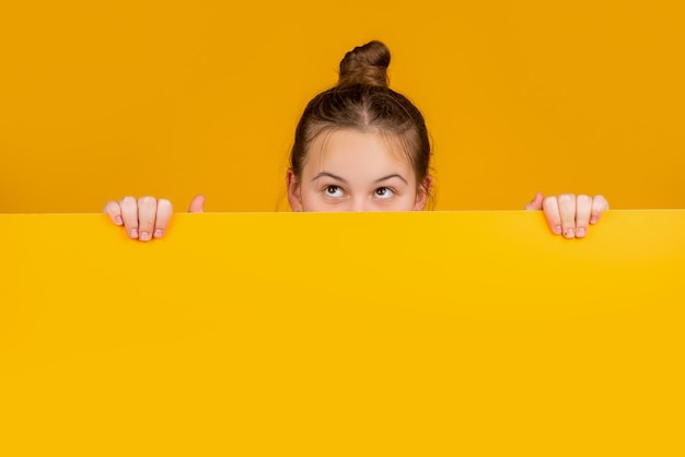 girl hiding behind yellow paper with copy space for advertisement