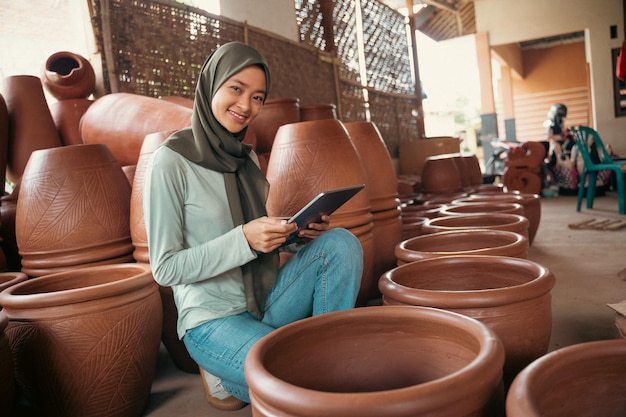 도자기 사이에 태블릿을 사용하여 웃는 히잡을 쓴 소녀