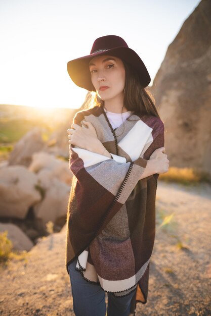 Girl hiker in poncho and hat on top of mountain at sunset