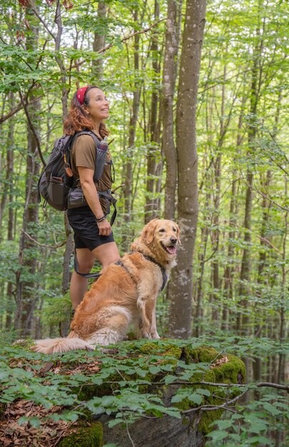 Girl hiker smiling with her golden retriever dog observes nature in forest