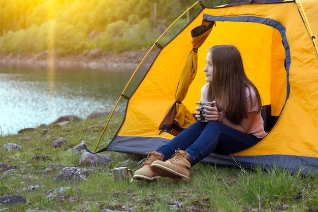 Girl hiker in a tent and holding a cup mountains in the background, norway