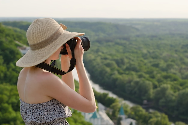 Girl on hill takes pictures against the background of a forest and meandering river