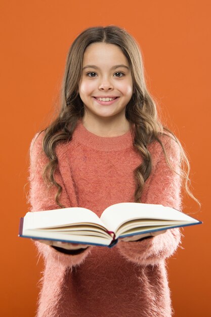 Girl hold book read story over orange background. Child enjoy reading book. Book store concept. Wonderful free childrens books available to read. Reading practice for kids. Childrens literature.