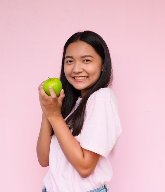 La ragazza tiene appel verde su sfondo rosa.