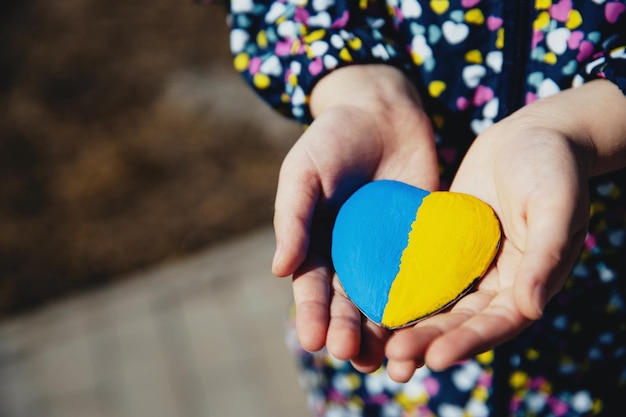 Foto ragazza tiene una pietra a forma di cuore con la bandiera blu-gialla dell'ucraina inno nazionale ragazza ama la patria natale