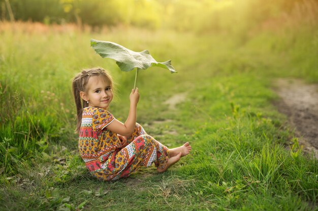 Girl hold large burdock leaf like umbrella.