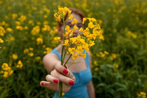 写真 野原で黄色い菜の花を持つ女の子