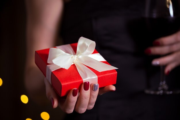 Girl holding beautiful  gift for the day valentines day. red box and white bow and bokeh in the background