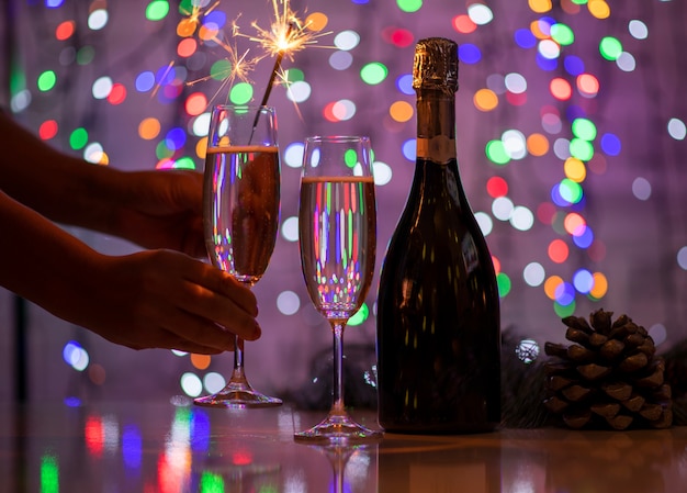 Girl holding a bengali fire and a glass of champagne on a beautiful festive bokeh lights