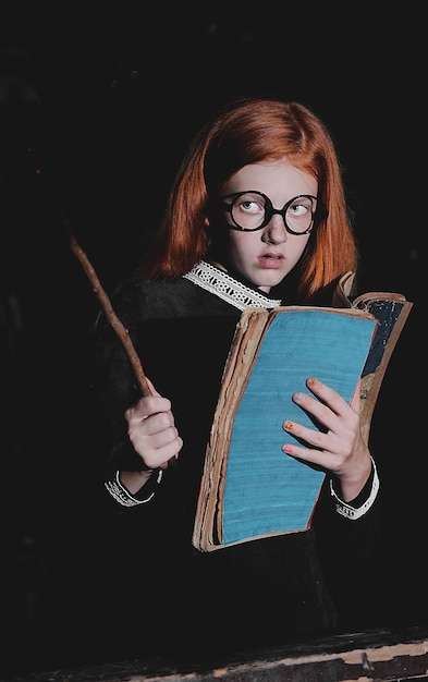 Girl holding book and stick against black background