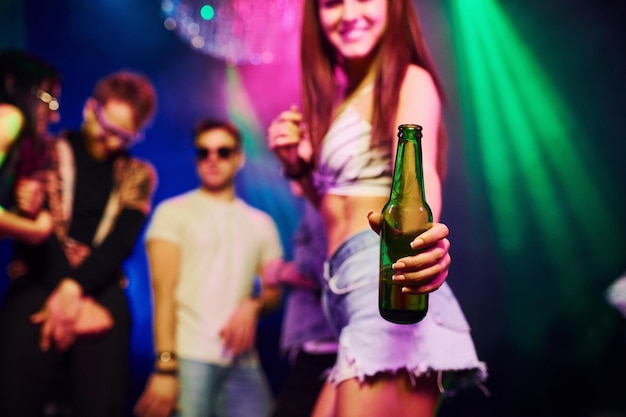 Girl holding bottle Young people is having fun in night club with colorful laser lights