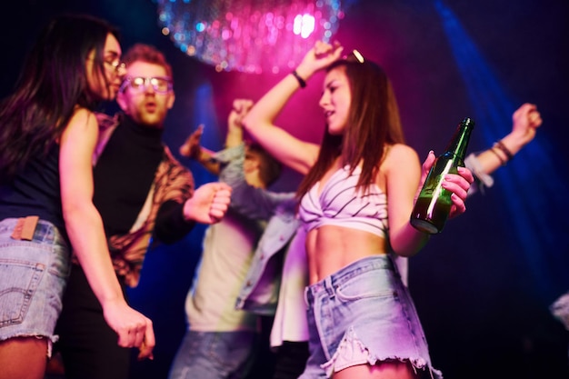 Girl holding bottle Young people is having fun in night club with colorful laser lights