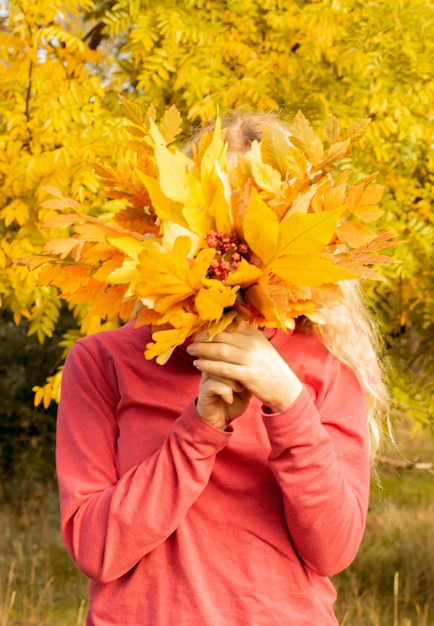 Girl holding a bouquet of autumn leaves covering her face. soft selective focus