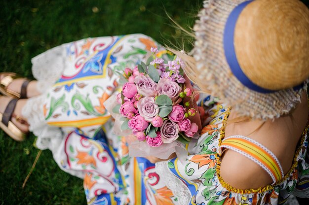 Girl holding bouquet of different pink flowers sitting on the grass