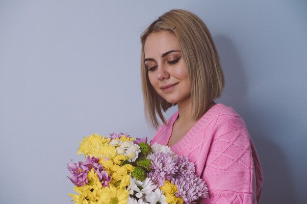 彼女の手に花束を持っている女の子。明るい背景、クローズアップの肖像画。休日、誕生日、女性の日の概念。