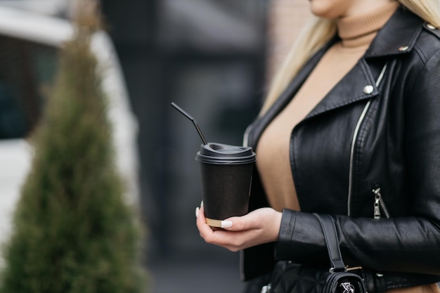 段ボールのカップを持っている女の子店の背景に女性の手で紙のコーヒーカップ熱い飲み物コーヒーの紙コップを持っている手紙のコーヒーカップ