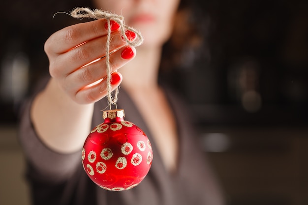 Girl holding Christmas ball in fingers. Beautiful manicure on a background of the red ball.