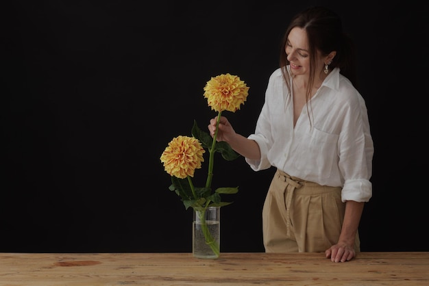 Girl holding a dahlia flower in a glass vase on a wooden table dark background mockup