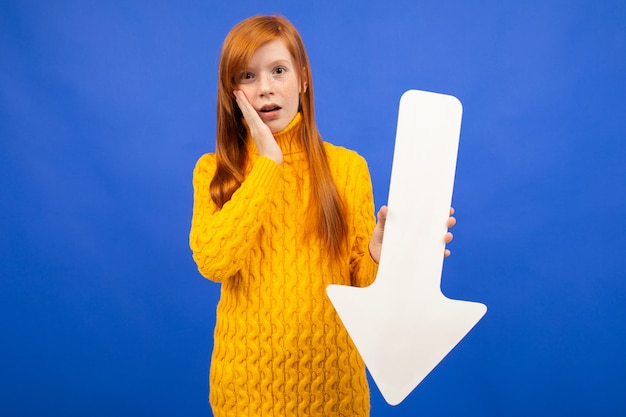 Ragazza che tiene una freccia giù da carta sull'azzurro