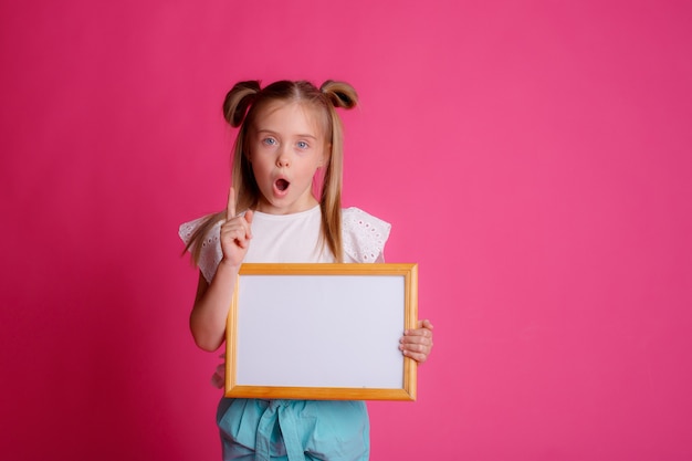 girl holding an empty frame, surprised, space for text Studio on a pink