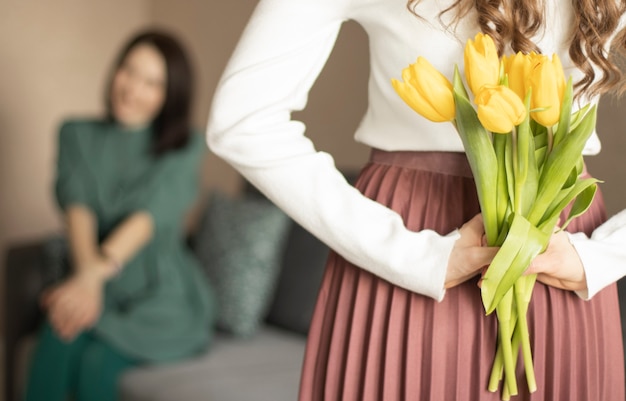 Girl holding flowers for mother behind her back, closeup