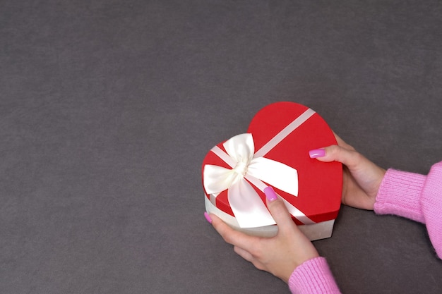 Girl holding a gift in a red box in the shape of a heart. Dark background, selective focus. Concept black friday, holiday, birthday, womens day.