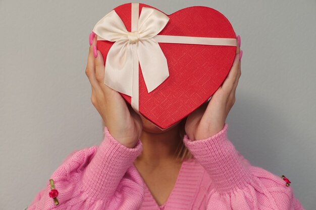 Ragazza con un regalo in una scatola rossa a forma di cuore. sfondo chiaro, messa a fuoco selettiva. concetto - venerdì nero, vacanza, compleanno, festa della donna.