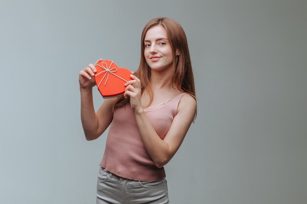 Ragazza con una confezione regalo a forma di cuore su sfondo grigio