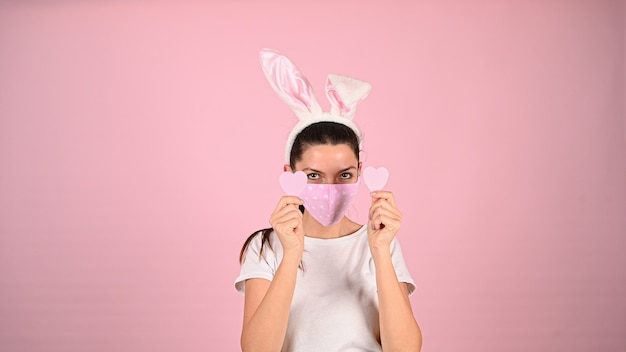 Girl holding a heart with her hands in a mask, on a pink background. High quality photo