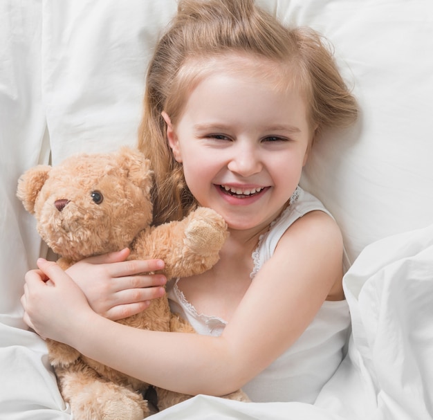 Girl holding her brown teddy, in bed