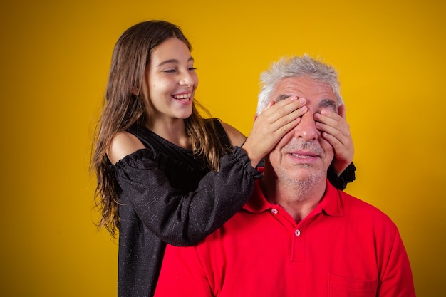 Girl holding her father closed eyes. yellow background. fathers Day. Brazilian family.