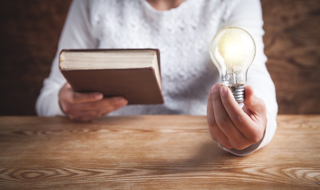 Ragazza che tiene la lampadina e il libro. conoscenza, creatività, saggezza