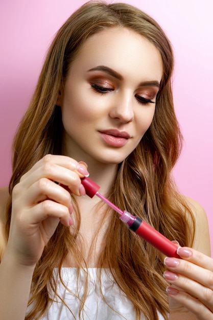 Girl holding lipstick on a pink background