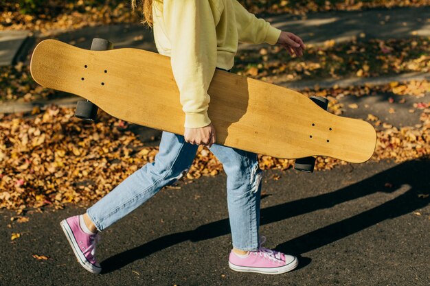 Girl holding a longboard while walking down the street with fall leaves in the background