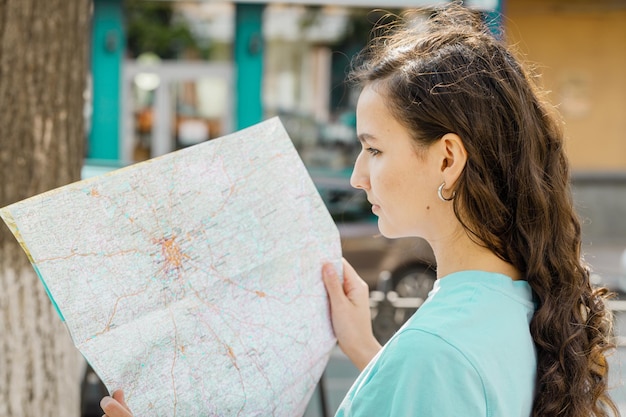 Foto ragazza che tiene la mappa turistica alla ricerca di un modo di viaggiare in piedi su sfondo bianco