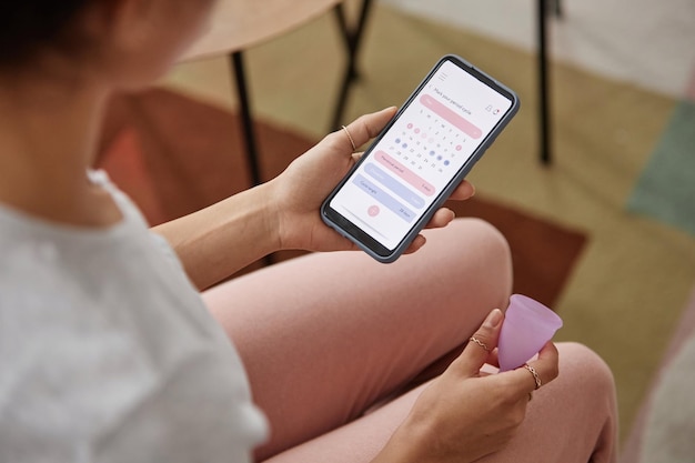 Girl holding menstrual cup and smartphone