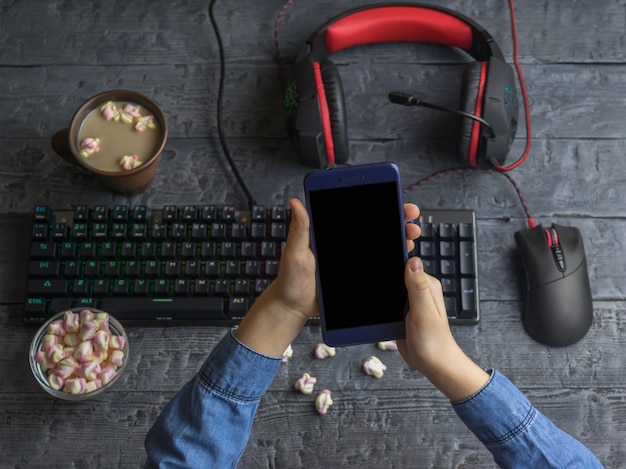 Girl holding a mobile phone on the background of computer accessories, coffee and marshmallows