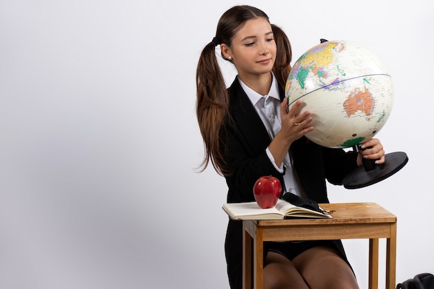 A girl holding a model of globe looks at it isolated on white blank space