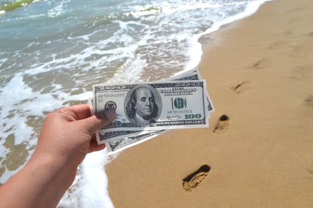 海を背景に300ドルの紙幣を持っている女の子