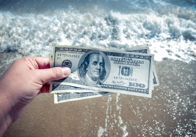 Girl holding a money bill of 300 dollars on background of sea waves