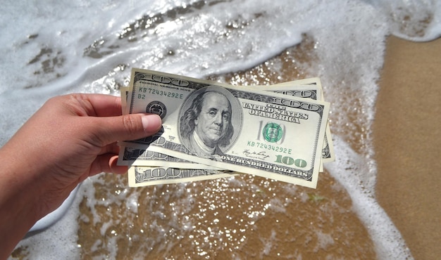 Photo girl holding a money bill of 300 dollars on background of sea waves