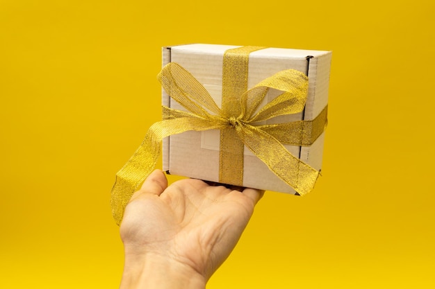 Girl holding a New Year's gift in a white box with a golden ribbon on a yellow background