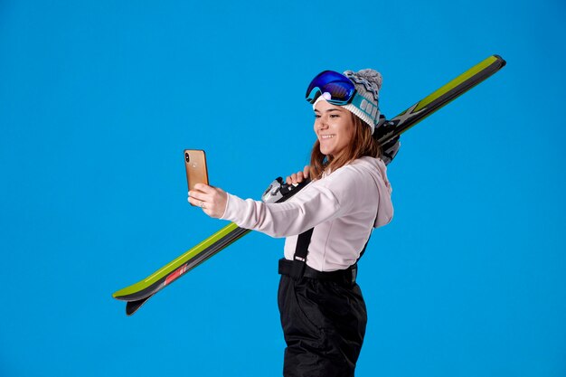 Girl holding a pair of skis taking a selfie while smiling