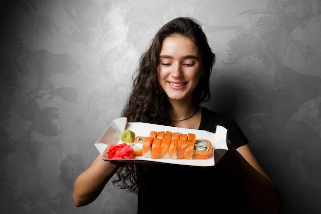 Ragazza con philadelphia rotoli in una scatola di carta su sfondo grigio. sushi, cibo a domicilio.