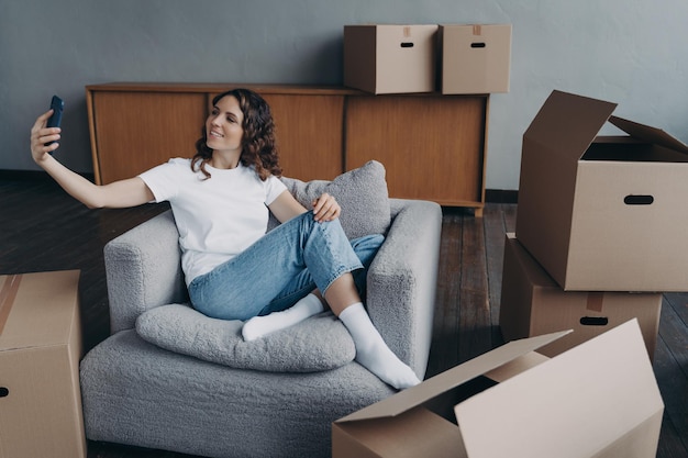 Girl holding phone communicates by video call showing house\
with cardboard boxes on moving day